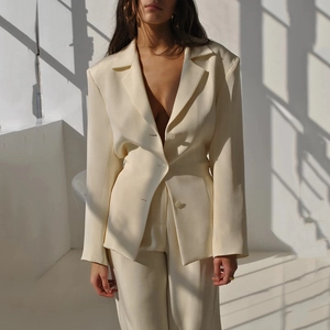 Detail of waist-contoured cream satin blazer featuring a smooth glossy finish and padded shoulders