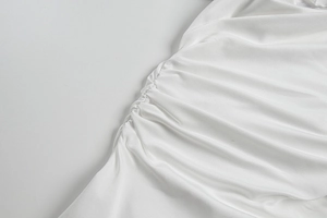 Détail de la robe en satin blanc montrant la texture lisse et le design plissé
