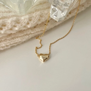 Close-up of a minimalist gold heart pendant necklace on a warm knitted background