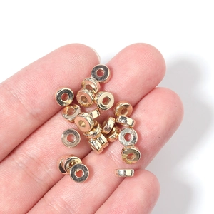 Close-up of golden CCB flat round spacer beads held in hand for jewelry size comparison