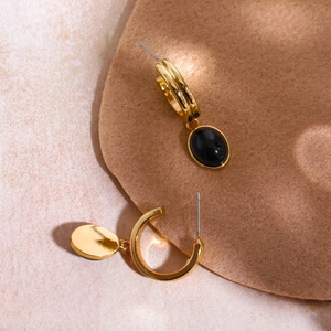 Macro shot of gold C-shaped hoop earrings with elegant black oval gemstone pendants