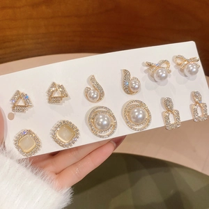 Close-up of gold ear studs set with opals, pearls and crystals in various geometric shapes