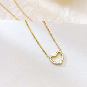 Elegant gold heart necklace with sparkling pavé crystals on textured white background