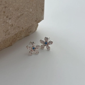 Silver flower stud earrings with hammered texture and a blue zircon center stone