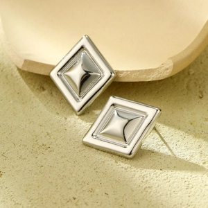 Macro shot of silver stainless steel geometric square stud earrings on stone