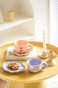 Creative hand-pinched ceramic tulip coffee cup and flower saucer set on a yellow table