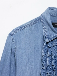 Detailed close-up of light blue denim shirt featuring ruffle accents and collar texture