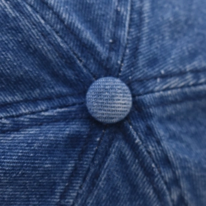 Detailed macro view of denim baseball cap crown showing fabric button and top stitching
