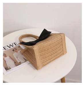 Detailed close-up of straw woven tote bag featuring a large black bow and round handle