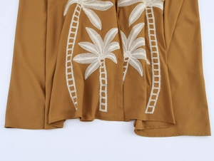 Gros plan détaillé d'une broderie de cocotier blanc sur une robe d'été caramel