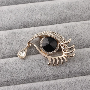 Detail shot of eye-shaped brooch with black gem and crystal teardrop on velvet tray