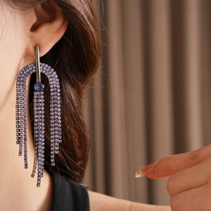 Close-up of long tassel earrings with purple crystals on a model in warm light