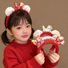 Detail view of a red plush hairband with festive folk patterns and white pom-poms
