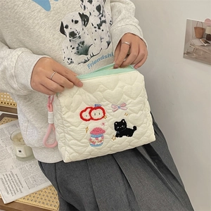 Detail of cream quilted makeup bag with cat and heart embroidery held by hands