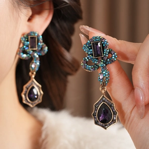 Détail de boucles d'oreilles vintage en bronze avec gouttes violettes et strass bleu-vert