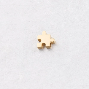 Macro d'un pendentif pièce de puzzle dorée sur fond marbre pour création de bijoux