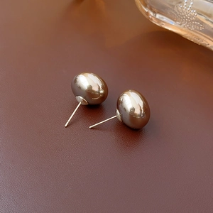 Macro shot of gold tone oval pearl earrings on a dark leather textured surface