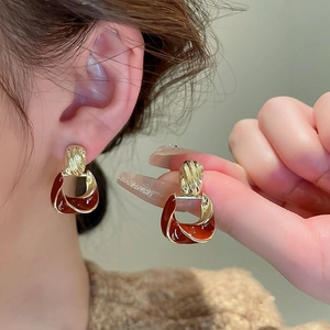 Close-up of golden geometric earrings with deep red enamel on a model's ear