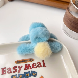Detail of blue plush hair claw clip with a contrast yellow pompom on a decorative plate