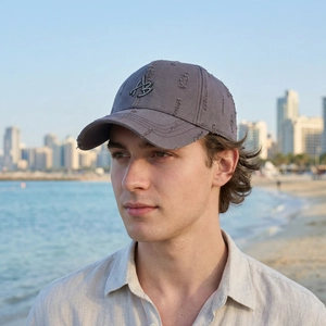 Distressed dark gray baseball cap with metal AB logo on sunlit urban beach background