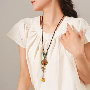 Ethnic style ceramic beaded necklace with leaf pendant worn by model on plain background