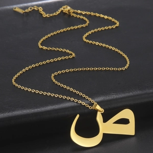 Detailed view of Arabic letter pendant on a gold chain over black leather background