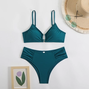 Flat lay of teal bikini set with gold ring detail, sun hat and sunglasses on white background