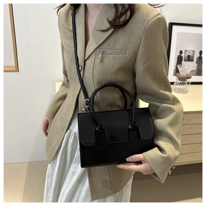 Chic black rectangular crossbody bag with dual handles shown in a minimalist interior