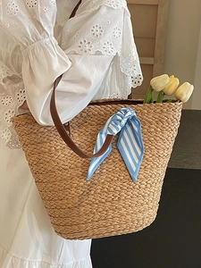 Minimalist straw tote bag with brown leather handles and blue scarf on a wooden surface