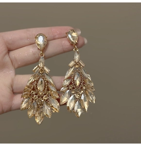Macro shot of champagne gold teardrop crystal earrings held by hand showing faceted shine