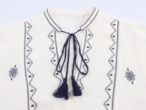 Detail of blue ethnic embroidery and tassel ties on a white cotton linen shirt