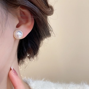 Close-up of model wearing elegant round pearl earrings with textured gold-plated edges