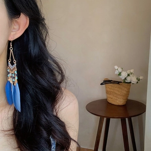 Blue feather tassel earrings in bohemian style worn by a model in a cozy home setting