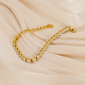 Goldenes Tennisarmband mit rechteckigen Zirkonia-Steinen auf cremefarbenem Satinstoff