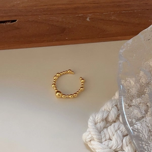 Detail of minimalist gold beaded open ring on a textured background with soft lighting