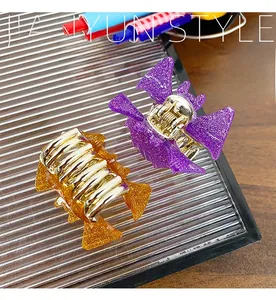 Detail of bat-shaped hair claws with glitter finish in purple and amber acrylic colors