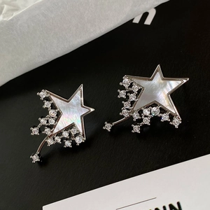 Macro detail of star-shaped earrings featuring mother of pearl inlay and zircon tassels