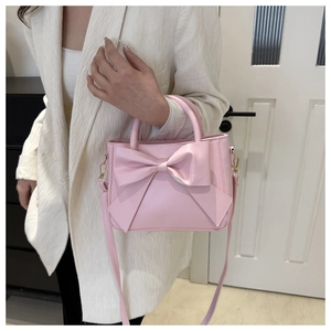 Detail of pink PU leather square bag featuring a large bow and detachable shoulder strap