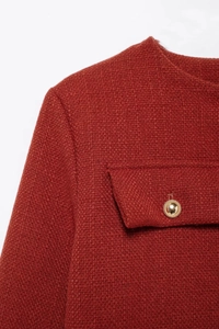 Détail du tissu en tweed rouge brique foncé avec un bouton en métal doré ornementé