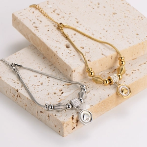 Elegant gold and silver snake chain bracelets with heart charms on beige stone