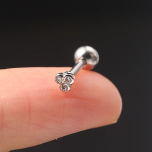 Macro shot of tiny silver piercing stud with three zircons held on a fingertip