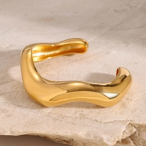 Minimalistischer goldener Wellenarmreif aus poliertem Edelstahl auf Steinsockel