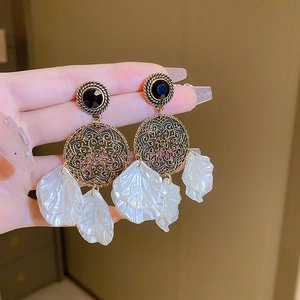 Détail de boucles d'oreilles ethniques avec ciselure métallique et pétales de nacre blanche