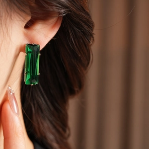 Detail of emerald green rectangular zircon earring worn by a model on warm background