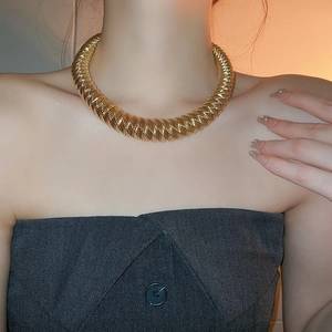 Close-up of a chunky golden woven collar necklace on a model in warm lighting