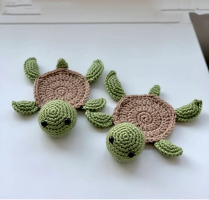 Detailed view of two handmade crochet turtle coasters with green heads and brown shells