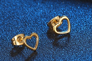 Macro shot of gold heart stud earrings with metallic luster on blue textured background