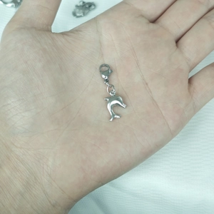 Macro shot of silver dolphin charm with lobster clasp shown on a palm for size reference