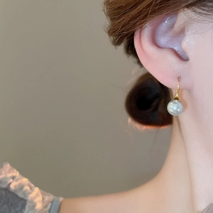 Close-up of elegant 18K gold pearl hook earring worn by a model in warm soft light