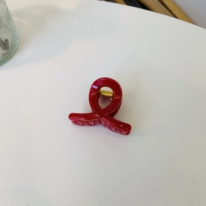 Detail of red resin shark hair claw clip with golden spring and minimalist cross design